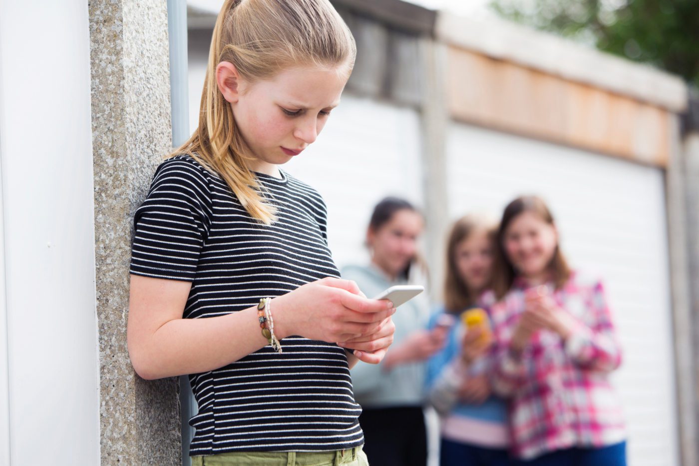 Image of a young person looking at her phone with bullies blurred out in the background